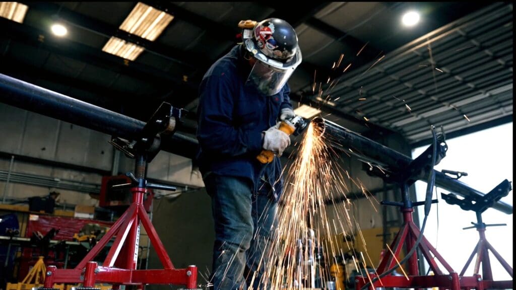 A man in blue jacket grinding metal with an angle grinder.