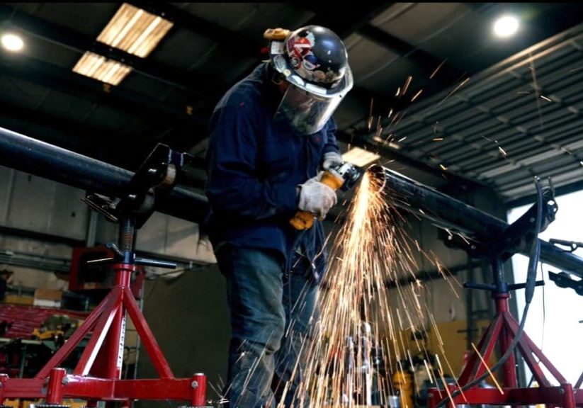 A man in blue jacket grinding metal with an angle grinder.